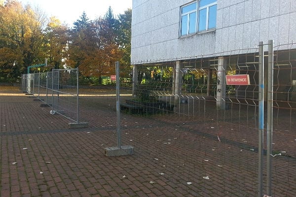 Der Schulhof des Berufkollegs ist mit einem Zaun abgetrennt. Ein Tor führt hindurch